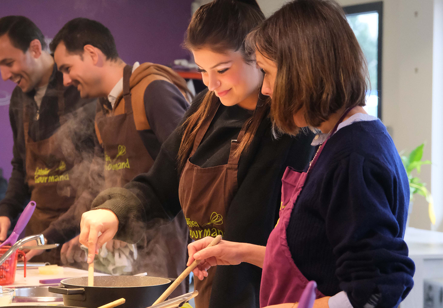 Deux femmes au premier plan et deux hommes en deuxième plan, faisant un cours de cuisine.